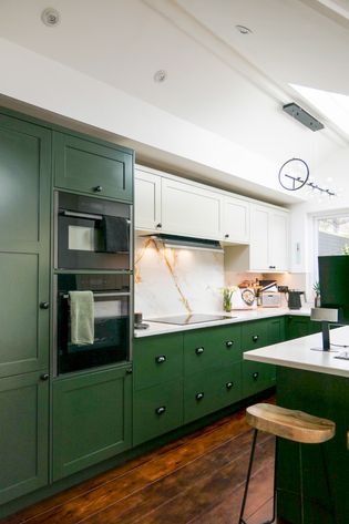 Dark green and cream shaker cabinetry in a u-shape layout, with a marble style worktop and spalshback