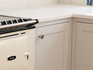 A sleek, shaker kitchen corner features a cream-colored AGA stove with a silver handle and adjacent light grey cabinets. The space feels clean and minimalist.