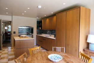 Modern walnut kitchen and dining area with a central island, round wooden table, and decorative bowl.