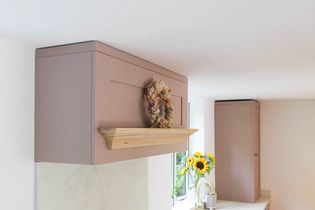 Simple kitchen interior with pastel pink cabinets. A wooden mantel features a dried floral wreath. A nearby vase holds bright sunflowers, adding a cheerful touch.
