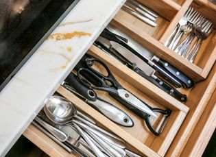 A wooden cutlery insert filled with all different silver kitchen utensils