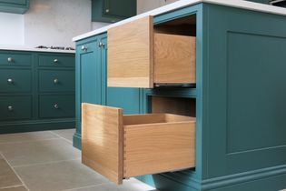 Kitchen with green cabinets and two open wooden drawers. The design is modern, with tiled floors and a light countertop, conveying a clean, spacious feel.