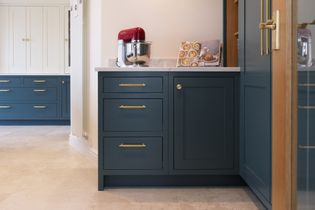 Shaker kitchen with blue cabinets and gold handles. A red stand mixer and an open cookbook rest on the marble countertop, creating a cozy and inviting atmosphere.