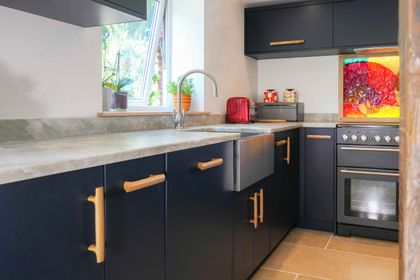 Navy slab kitchen run with oak bar handles, a stainless sink and a range cooker