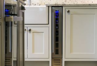 Light grey kitchen cabinets with sleek handles, featuring a narrow wine fridge with a blue interior light, create a modern, elegant ambiance.