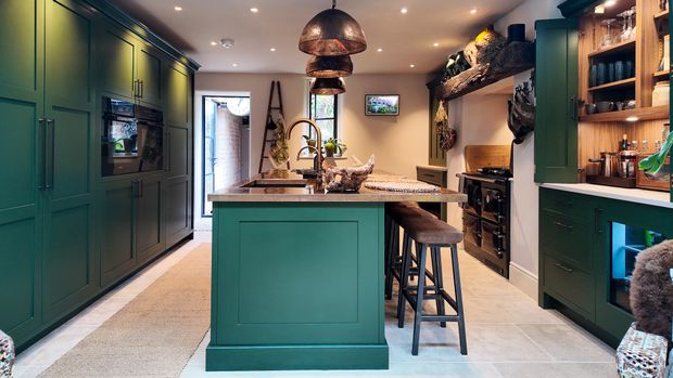 Dark green Shaker kitchen with a copper island, open shelving, stools, and warm pendant lighting.