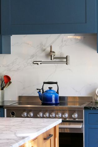 A blue kettle on a stovetop with a marble backsplash and grey cabinetry.