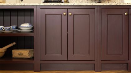 Hand-painted deep burgundy Shaker cabinets with a brass knob and a speckled granite worktop
