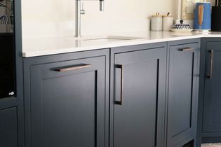 Stylish kitchen with matte blue cabinets and sleek, metallic handles. Features a white countertop, stainless steel tap, and neatly arranged kitchen items.