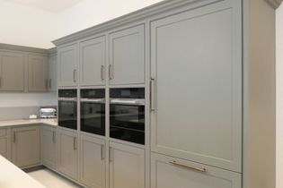 Sleek kitchen with light grey cabinets, a stainless steel double oven, and built-in fridge. Warm, modern ambiance with subtle elegance.