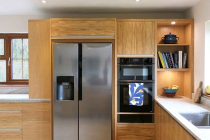 Oak cabinetry housing an American-style fridge-freezer, integrated ovens and open bookshelves