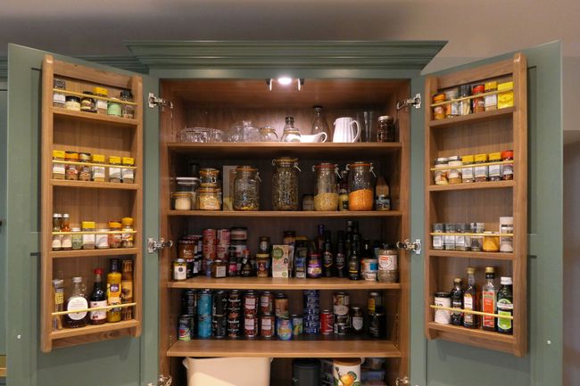 Open pantry cupboard with neatly organized shelves. Jars of grains, spices, canned goods, and bottles fill the space, conveying order and abundance.