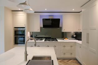 Shaker kitchen with white cabinets, stainless steel appliances, and wooden flooring. Includes a central island sink and a bowl of oranges.