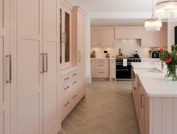 A large blush pink Shaker kitchen with a large curved island, black range and various appliances on the worktop.
