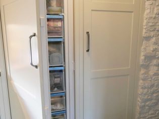 A white kitchen cabinet with a narrow, pull-out pantry door partially open, revealing shelves of organized containers. Bright, clean, and modern setting.
