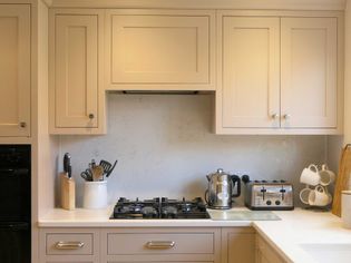 Shaker kitchen with neutral cabinets and a white countertop. Features a gas stove, kettle, toaster, knife block, and mugs, creating a tidy and inviting space.