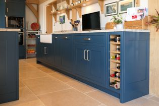 Stylish kitchen with blue cabinets, a marble countertop, and a built-in wine rack. Warm lighting creates a cozy, modern atmosphere.