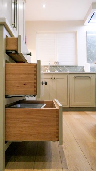 A Shaker kitchen with open wooden drawers in a off white cabinet, featuring a countertop and sink in the background.
