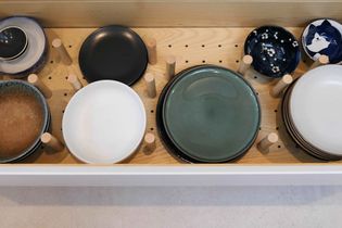 Neatly organized drawer with various plates and bowls of different colors and sizes, separated by wooden pegs on a light wood base.