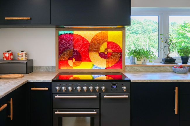 Close up of a red and yellow abstract splashback behind the range over with navy blue cabinets above ands below