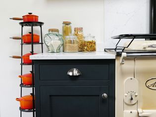 Kitchen corner with vibrant red pots on a vertical rack, jars of grains and pasta on a white countertop, and a classic cream stove, conveying coziness.