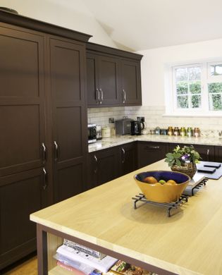 A Shaker kitchen with dark red cabinets, a granite countertop, and a kitchen island displaying a bowl of fruits.