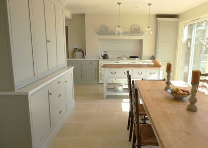Bright traditional kitchen with pale Shaker cabinetry, a central island, a tiled splash back, and a wooden dining table with candles and a bowl of apples.