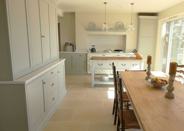 Bright traditional kitchen with pale Shaker cabinetry, a central island, a tiled splash back, and a wooden dining table with candles and a bowl of apples.