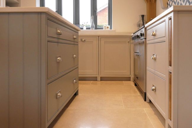 Shaker kitchen with light grey cabinets, sleek drawers, and stainless steel appliances. Large windows offer natural light, creating a warm, inviting tone.