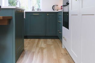 Shaker kitchen with green cabinets, quartz worktop and light wood flooring. Stainless steel kettle and window view add a fresh, inviting atmosphere.