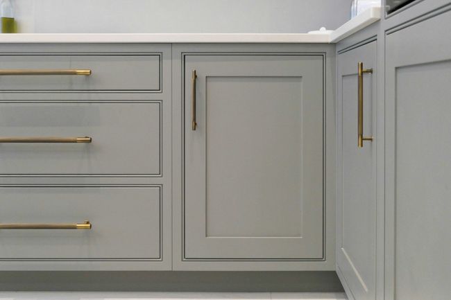 Grey kitchen cabinets with long, sleek bronze handles and a quartz worktop. The design is modern and minimalistic, conveying elegance and simplicity.