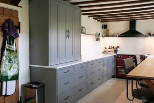 Shaker kitchen with grey cabinets, wooden beams, and red range. Aprons hang on a wooden door. Bright, inviting atmosphere with sleek design.