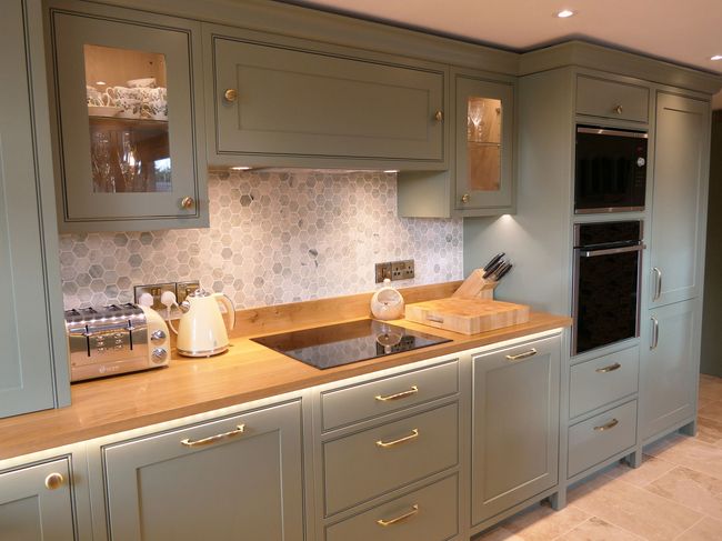 Shaker kitchen with green cabinets, wood countertops, and honeycomb tile backsplash. Includes appliances like a toaster, kettle, and built-in oven.