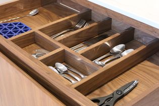 Open wooden kitchen drawer organiser containing assorted silverware, and a blue compartmented tray.