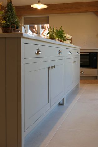 Shaker kitchen with a light island featuring sleek silver handles. Decor includes a potted plant and flowers, with warm, natural lighting.