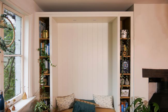 Shaker style reading nook with cushions, surrounded by bookshelves and plants. Soft lighting and greenery create a warm, inviting atmosphere.