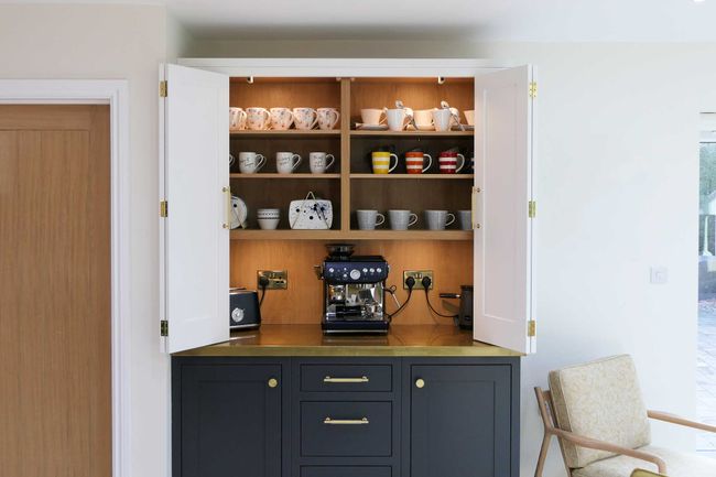 Open cabinet with neatly arranged mugs and cups on wooden shelves above a sleek espresso machine on a dark counter.