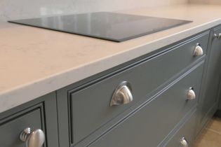 Sleek shaker kitchen with grey cabinets featuring metallic handles, and a smooth white countertop with an integrated black glass stovetop.