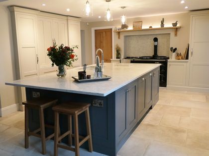 Shaker kitchen with a dark central island and neutral perimeter cabinetry. Pendant lighting is above the island with a vase of flowers in the centre. 