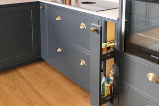 Sleek kitchen with dark grey cabinets, brass handles, and hardwood floor. A narrow pull-out spice rack is partially open next to an oven.