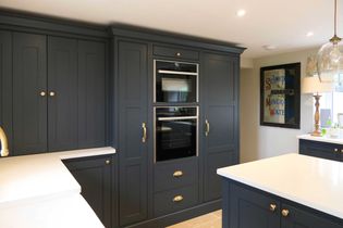 Sleek shaker kitchen with dark grey cabinets and bronze handles, featuring built-in double ovens. Bright white countertops contrast with the dark tone.