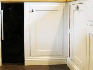 A white kitchen cabinet with a matte black refrigerator on the left. The cabinet has minimalist silver handles, conveying a sleek, modern look.