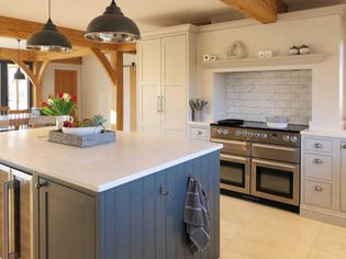 Spacious kitchen with light perimeter cabinetry, large island, and rustic beams. Features a modern stove, pendant lights, and fresh tulips, creating a warm, inviting atmosphere.