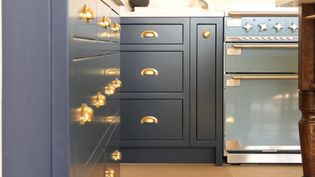 Stylish kitchen with navy blue cabinets, brass cup handles, and a light blue vintage oven. The design feels elegant and modern.