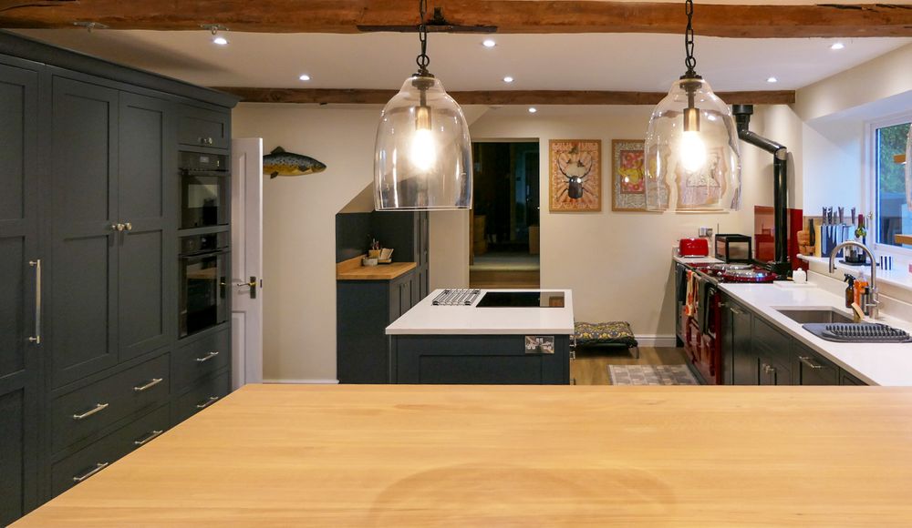 Shaker kitchen with dark cabinetry, a white island and countertops, glass pendant lights, exposed beams, and a sink beneath a window.