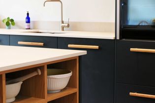 Dark blue modern kitchen, island with open wooden shelving at one end. Sink in the background.