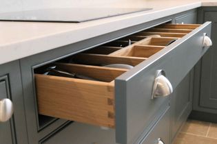 A grey kitchen drawer is open, revealing organized wooden compartments with silver handles. It creates a modern, tidy, and functional look.