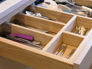 Wooden kitchen drawer open, showing organized silverware and utensils. Forks, spoons, and knives neatly placed in compartments.
