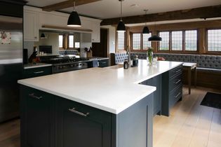 Spacious kitchen with a large island, dark cabinetry, and pendant lights. Windows with bench seating add warmth and natural light.