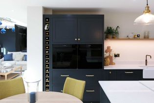 Shaker kitchen with dark cabinets, built-in ovens, and wine storage. A wooden shelf with plants and vases adds a touch of warmth.